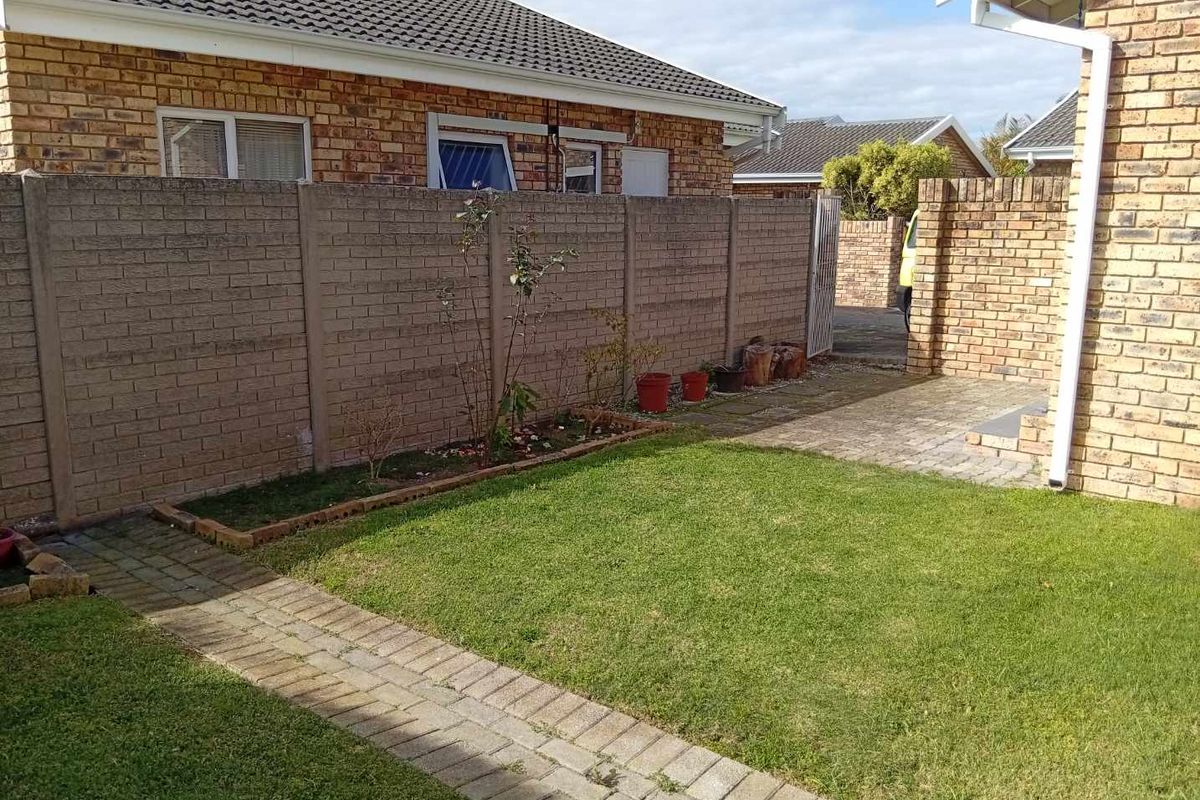 A private rear garden area featuring a well-maintained lawn, brick paved pathways, and secure precast concrete boundary walls.