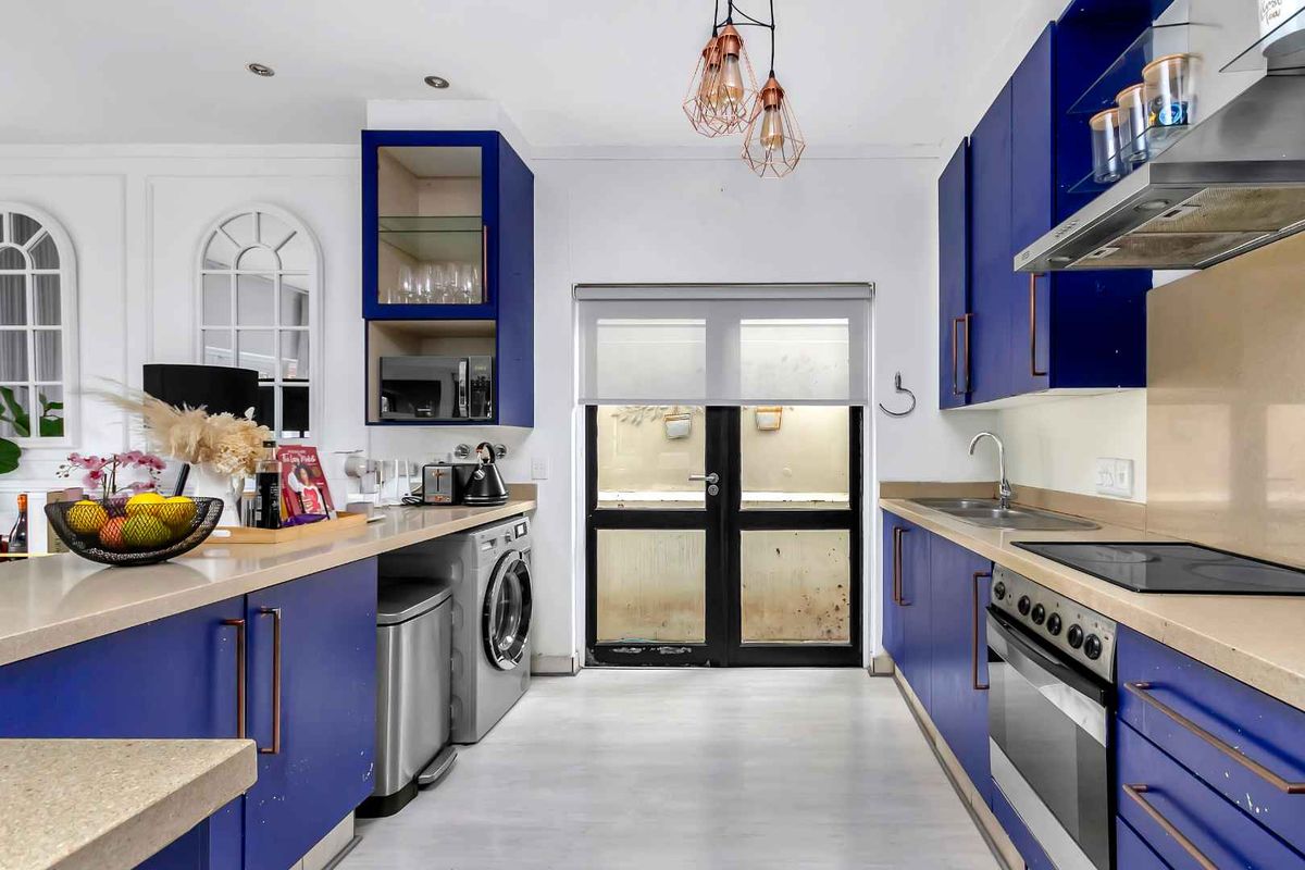 Modern kitchen featuring vibrant blue cabinetry, stone countertops, integrated oven, hob, extractor fan, and a dedicated space for laundry appliances.