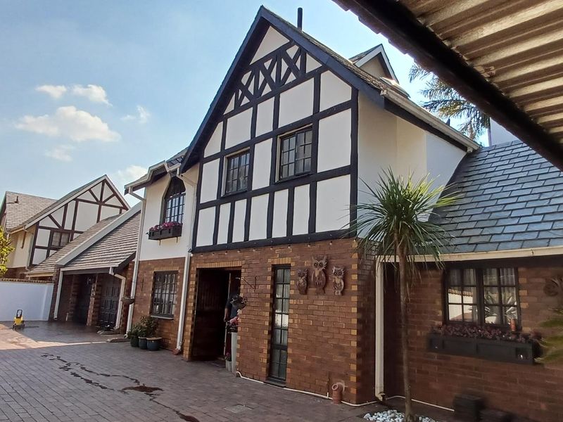 A charming Tudor-style house featuring a distinctive timber-framed facade, face-brick exterior, and a well-maintained paved driveway with covered parking.