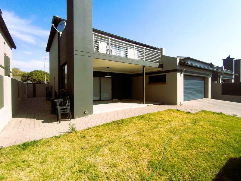 Rear view of the townhouse featuring a covered patio, upper-level balcony with metal railing, paved area, and a single garage.