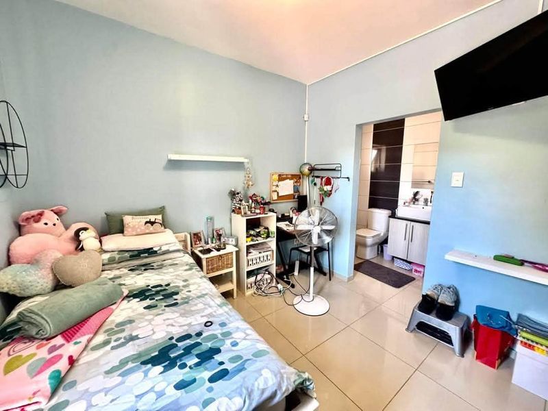 A bedroom featuring tiled flooring and an attached en-suite bathroom with a vanity and toilet.