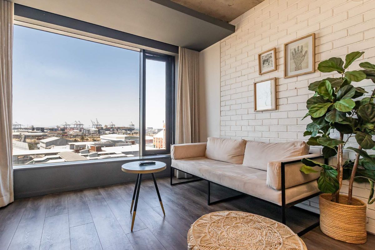 A modern living room featuring a large floor-to-ceiling window with expansive industrial views, exposed brick wall, and sleek laminate flooring.