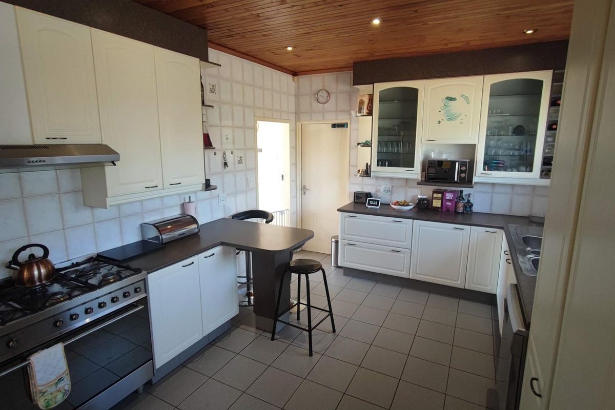 A functional kitchen featuring white cabinetry, a gas stove with extractor fan, tiled flooring, and a timber-paneled ceiling with recessed lighting.