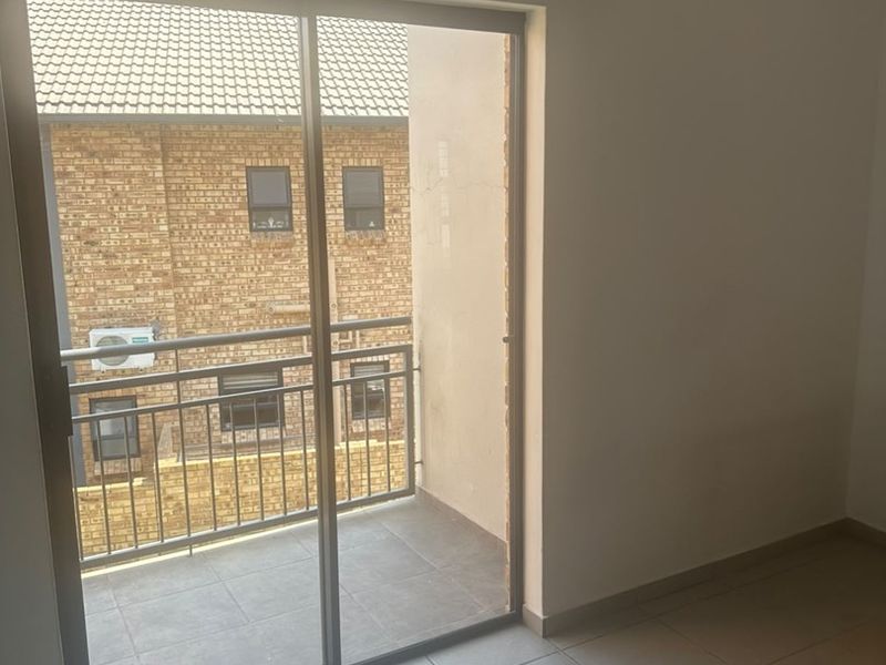 An empty bedroom featuring tiled flooring and a sliding glass door that opens onto a private balcony.