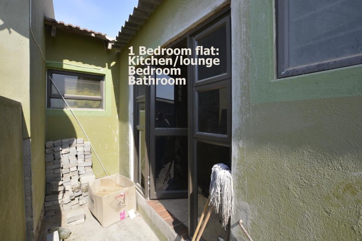 Exterior view of a flat entrance featuring dark-framed glass doors and unfinished exterior wall surfaces.