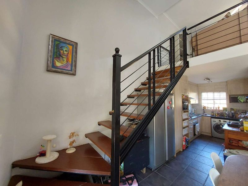 Open plan living area featuring a wooden staircase with metal balustrade leading to a mezzanine level, adjacent to a functional kitchen with tiled flooring.