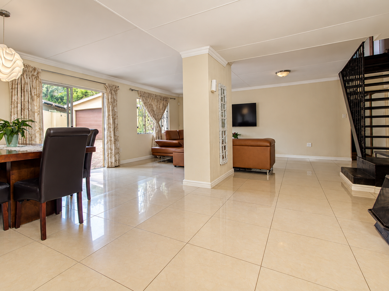 Spacious open-plan living and dining area featuring large porcelain tiles, a modern metal staircase, and a built-in fireplace with direct access to the patio.