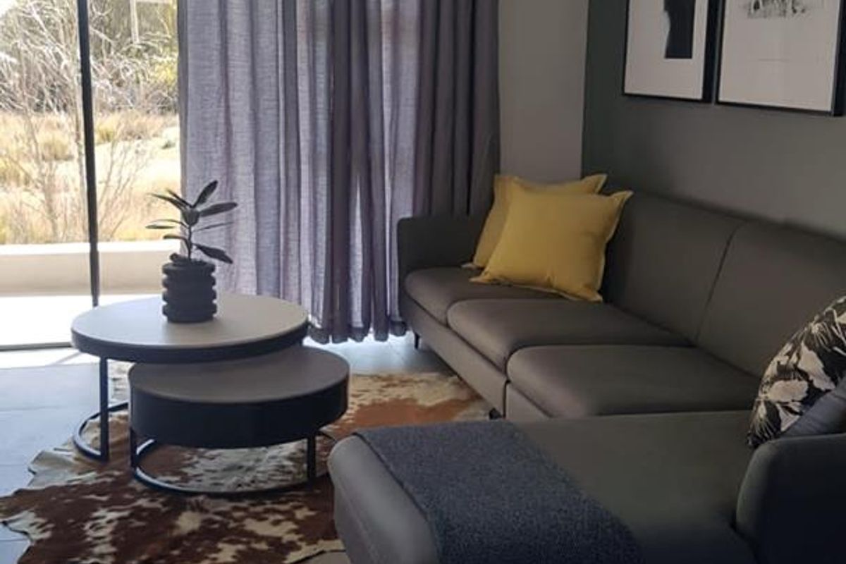 A modern living room featuring large format floor tiles, a sliding glass door leading to an outdoor area, and a neutral grey accent wall.
