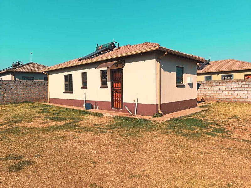 Rear view of the house featuring a tiled roof, solar water heater, and a secure entrance door, set within a fenced yard.