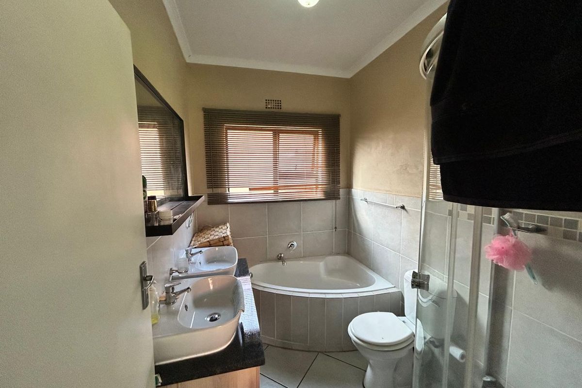 A functional bathroom featuring a corner bathtub, a glass-enclosed shower, and a double vanity with granite countertop.