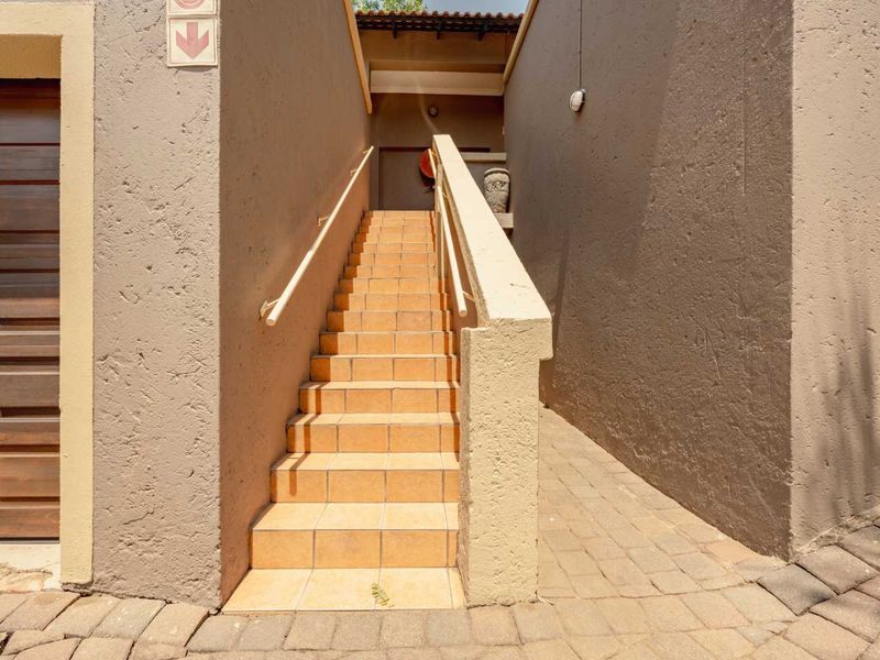 Exterior view of a townhouse entrance featuring a tiled staircase with a handrail, adjacent garage door, and paved driveway access.
