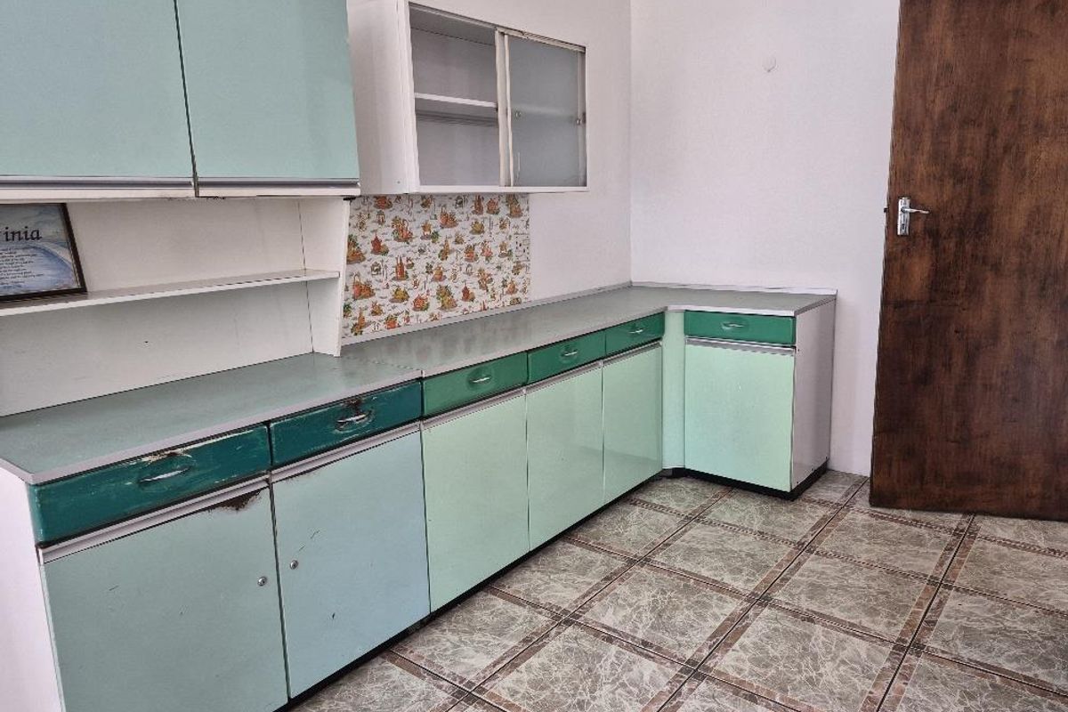 A dated kitchen featuring retro green cabinetry, laminate countertops, and patterned tile flooring, offering a blank canvas for modern renovation.