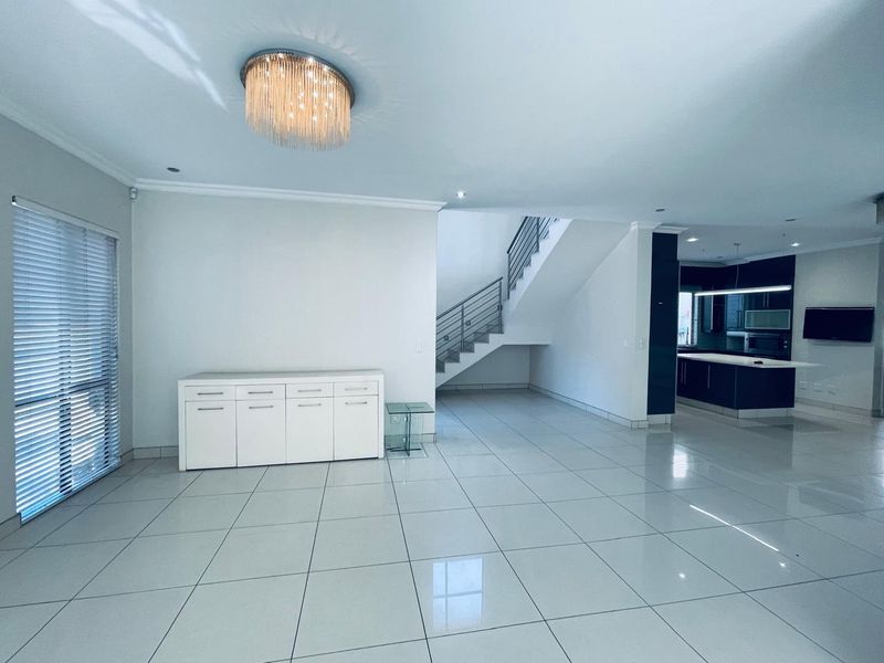 Spacious open-plan living area featuring polished tile floors, a modern staircase with metal balustrades, and a sleek kitchen with dark cabinetry.