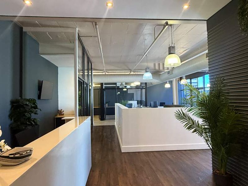 Modern open-plan retail or office space featuring high-quality laminate flooring, exposed concrete ceilings, glass partitions, and contemporary recessed and pendant lighting.