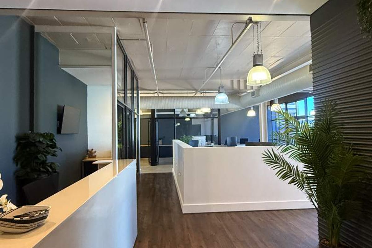 Modern open-plan retail or office space featuring high-quality laminate flooring, exposed concrete ceilings, glass partitions, and contemporary recessed and pendant lighting.