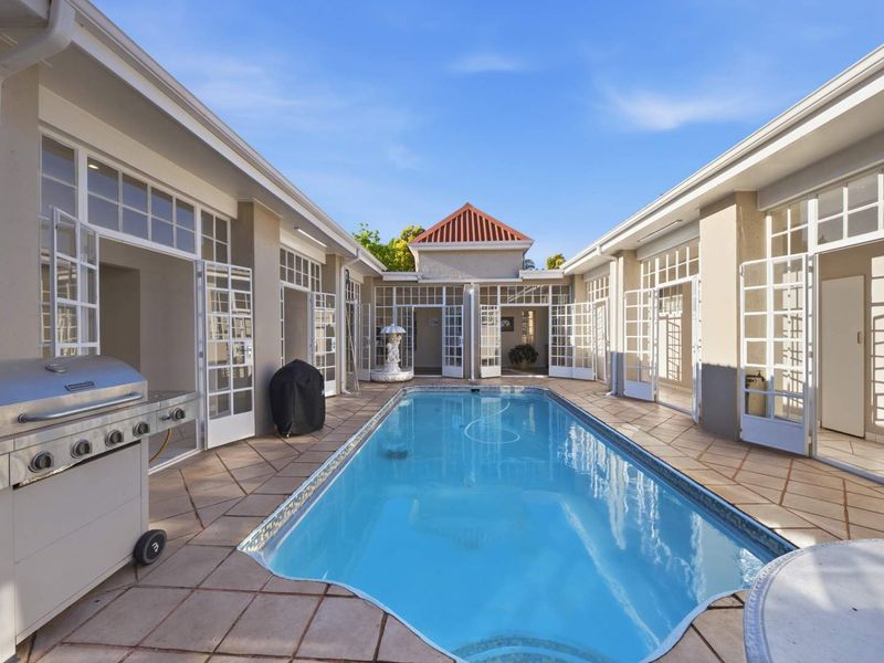 A central swimming pool courtyard surrounded by multiple sets of white french doors, featuring tiled flooring and a well-maintained pool structure.