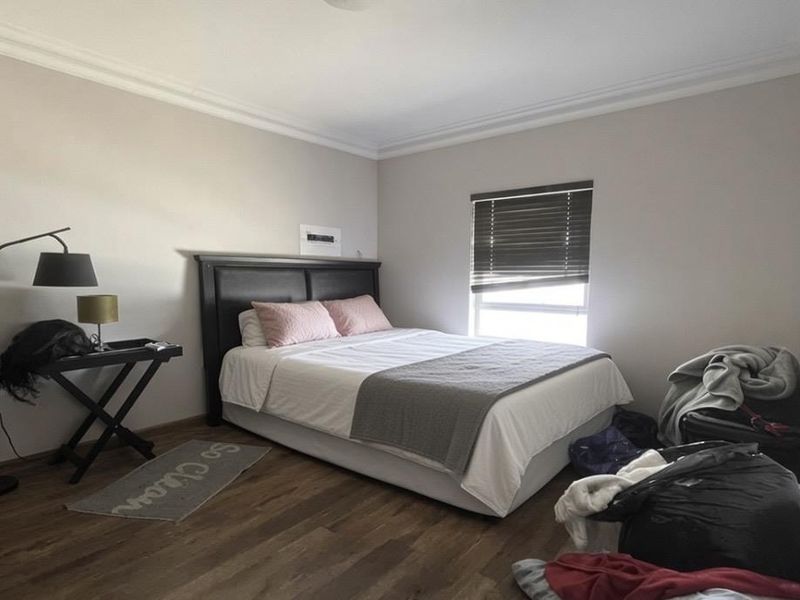 A bedroom featuring laminate flooring, crown molding, and a window fitted with venetian blinds.
