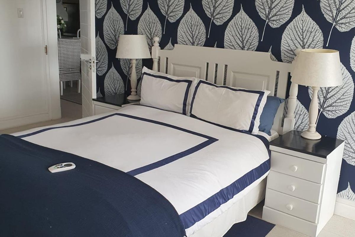 A well-maintained bedroom featuring a bold patterned feature wall, neutral carpeting, and a classic interior door leading to an adjacent living space.