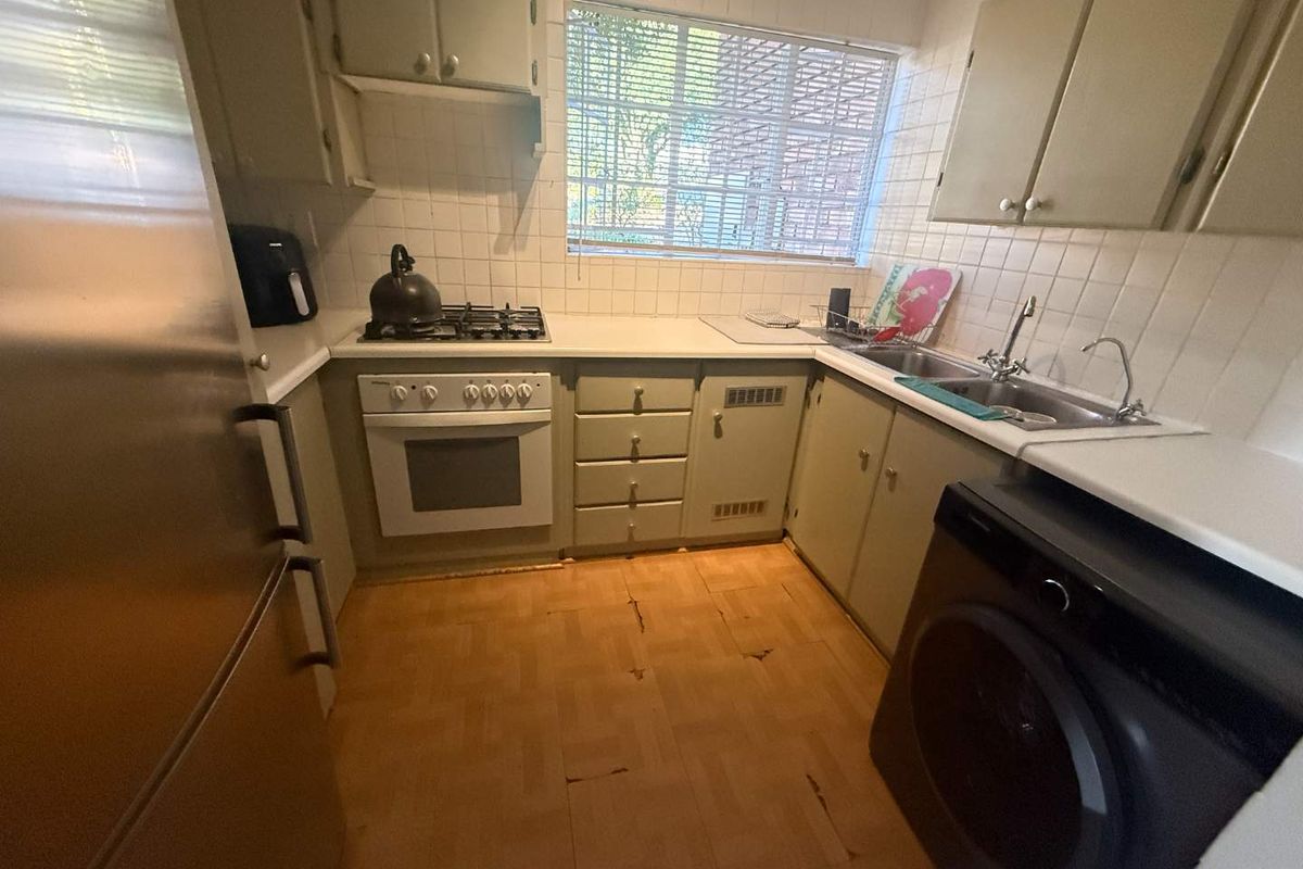 A compact kitchen featuring dated cabinetry, a built-in oven and gas hob, tiled splashbacks, and integrated laundry plumbing.