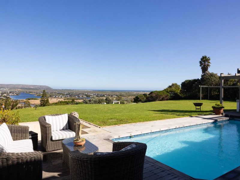 Outdoor pool area featuring timber decking, a pergola, and a spacious lawn with expansive coastal and landscape views.
