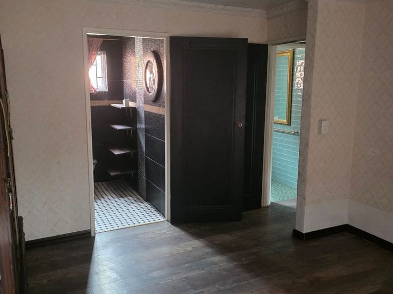 An empty bedroom featuring dark laminate flooring, crown molding, and recessed lighting, with direct access to two separate tiled bathroom areas.