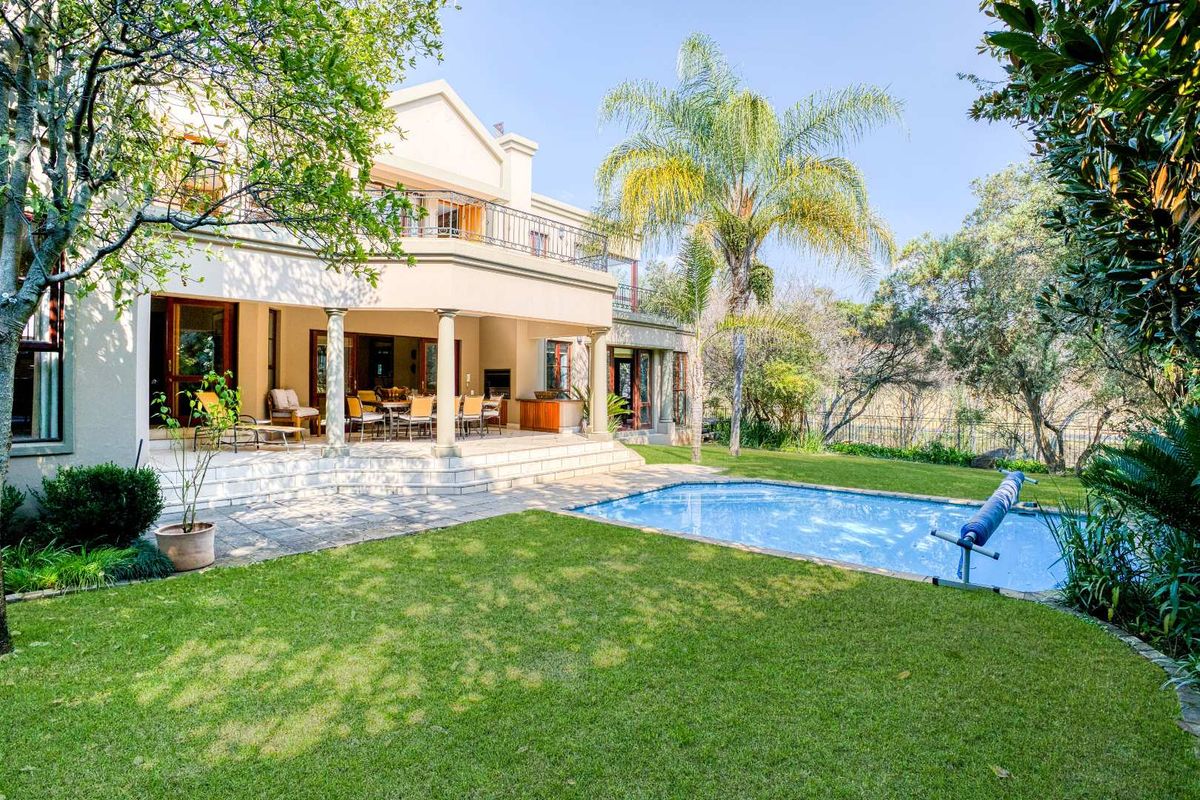 Spacious rear exterior featuring a covered patio with built-in braai, a swimming pool, and a well-maintained garden with a balcony above.
