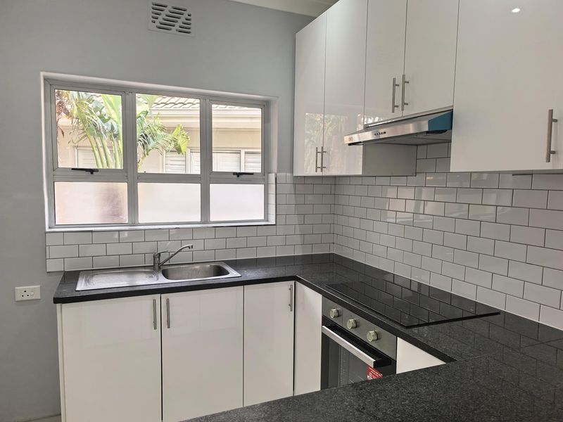 Modern kitchen featuring white gloss cabinetry, black granite countertops, subway tile backsplash, and integrated stainless steel appliances.