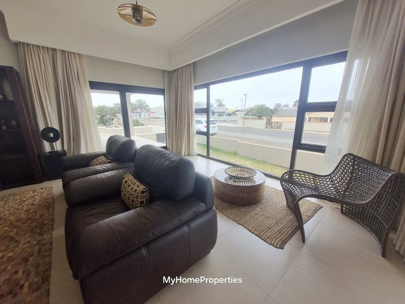 Bright living room featuring large aluminium-framed windows that provide ample natural light and views of the street.