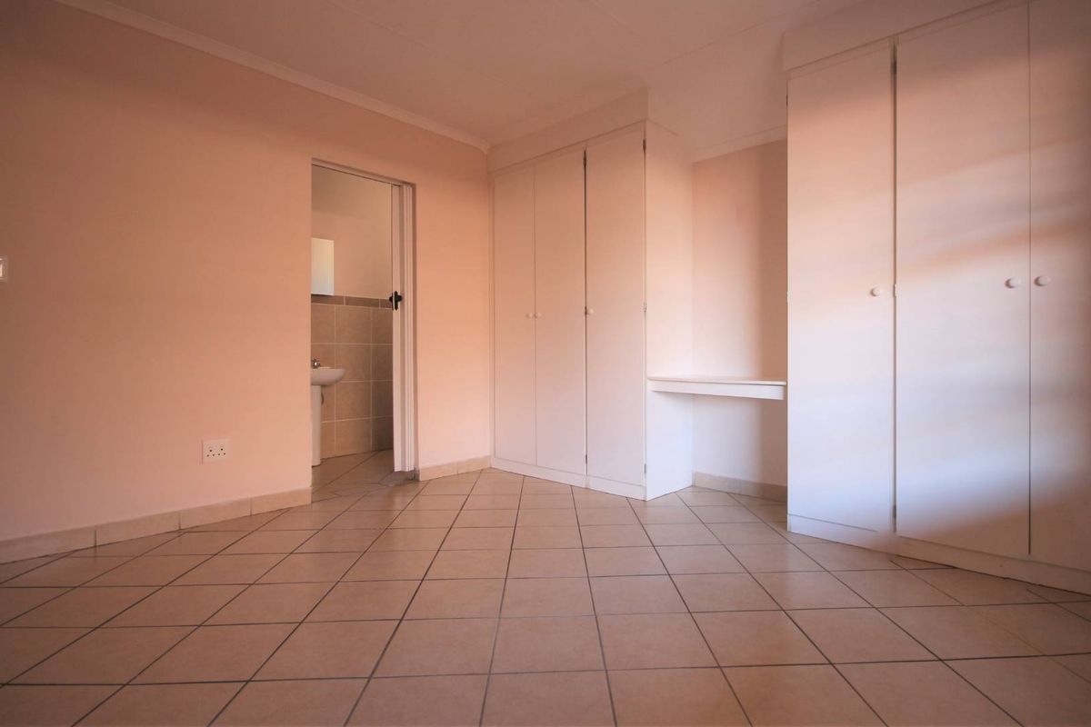An empty bedroom featuring tiled flooring, built-in cupboards with a vanity area, and direct access to an en-suite bathroom.