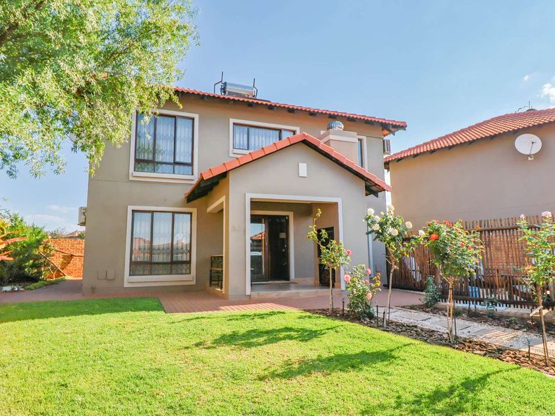 A well-maintained rear exterior view of the house featuring a paved patio, landscaped garden, and solar water heating system on the tiled roof.