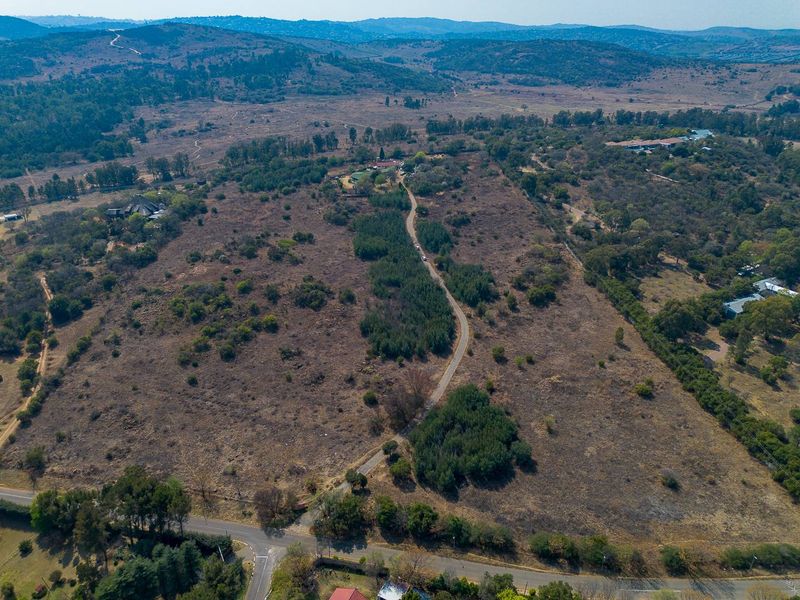 An aerial view of a large, undeveloped residential land parcel featuring natural vegetation and an existing access road.