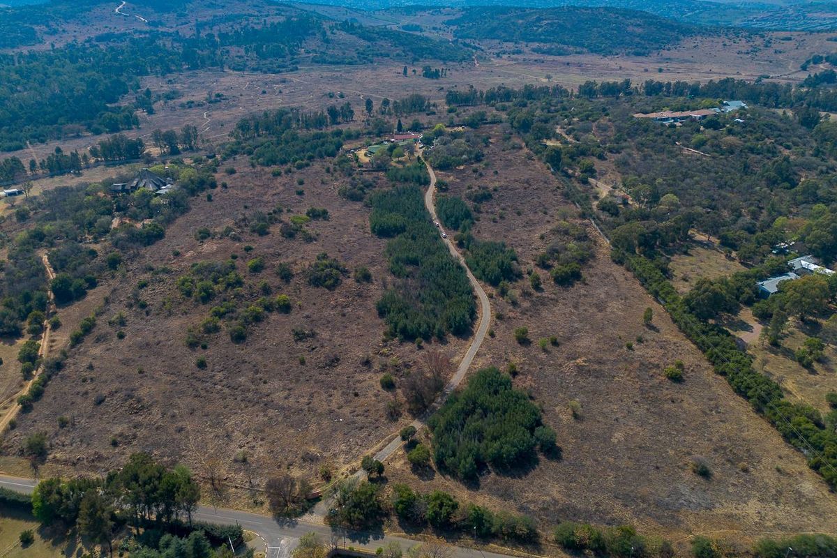 An aerial view of a large, undeveloped residential land parcel featuring natural vegetation and an existing access road.