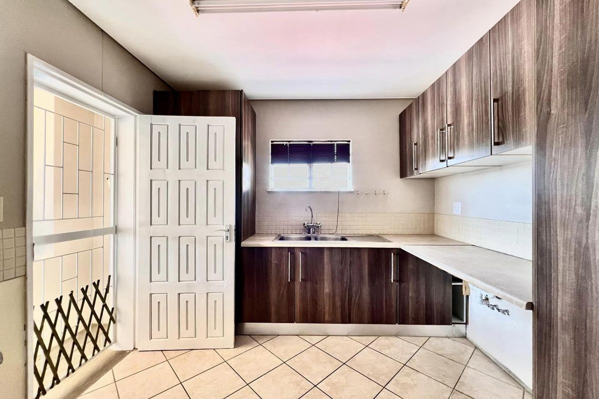 A functional kitchen featuring dark wood-look cabinetry, laminate countertops, a stainless steel sink, and tiled flooring with direct access to an exterior area.