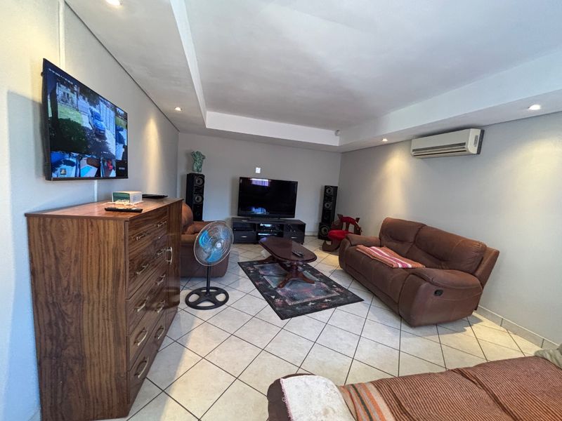 A spacious living room featuring tiled flooring, recessed ceiling lighting, and a wall-mounted air conditioning unit.