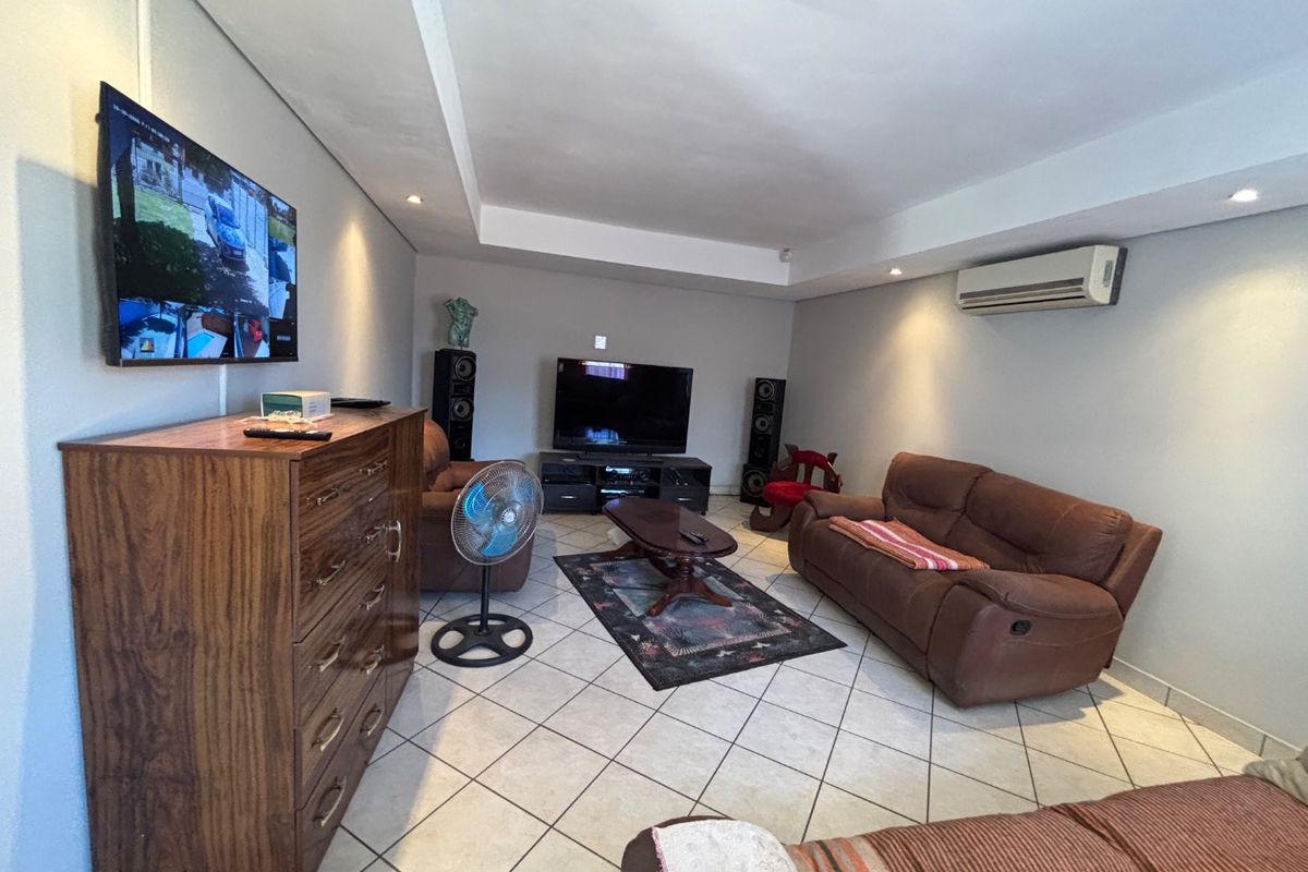 A spacious living room featuring tiled flooring, recessed ceiling lighting, and a wall-mounted air conditioning unit.