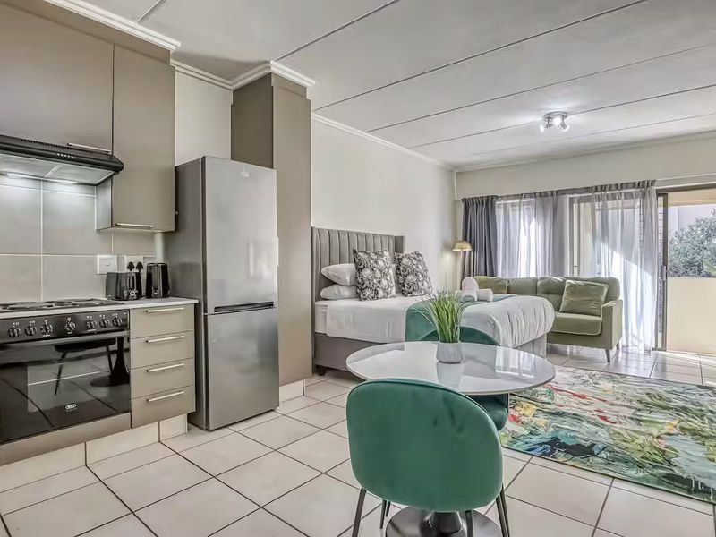 Open-plan studio apartment featuring a modern kitchen with built-in cabinetry, tiled flooring, and direct access to a private balcony through sliding glass doors.