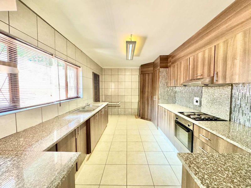 A spacious, well-maintained kitchen featuring granite countertops, ample built-in cabinetry, a built-in oven, electric hob, and tiled finishes throughout.