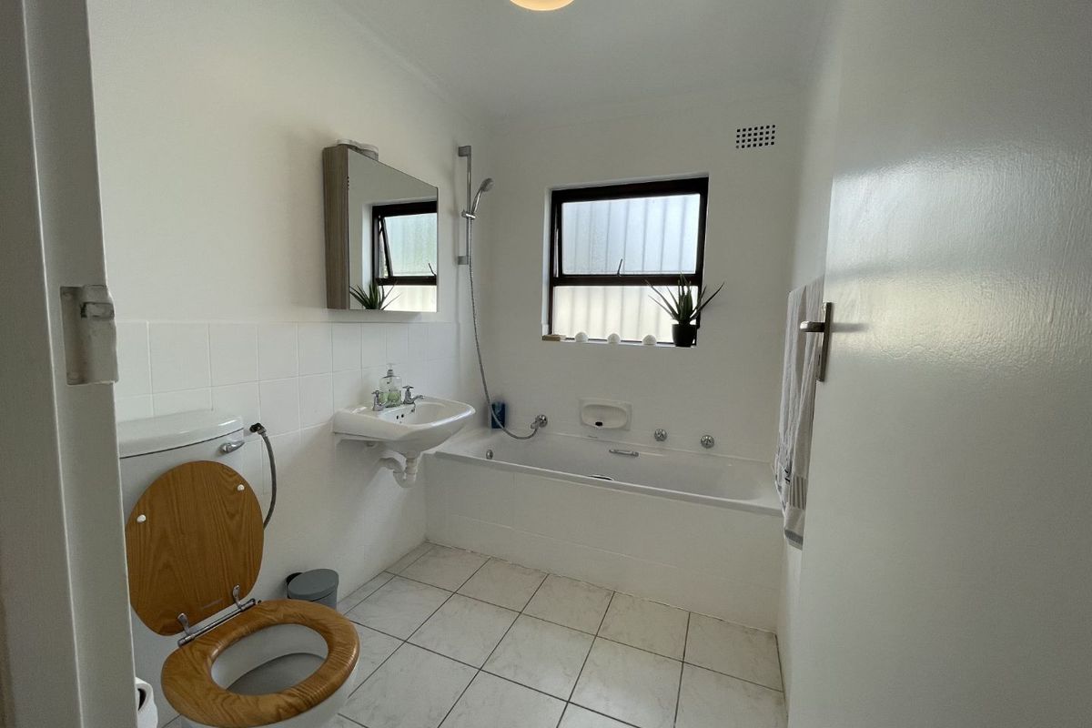 A functional bathroom featuring a bathtub with shower mixer, wall-mounted basin, and tiled finishes, offering a clean and practical layout.