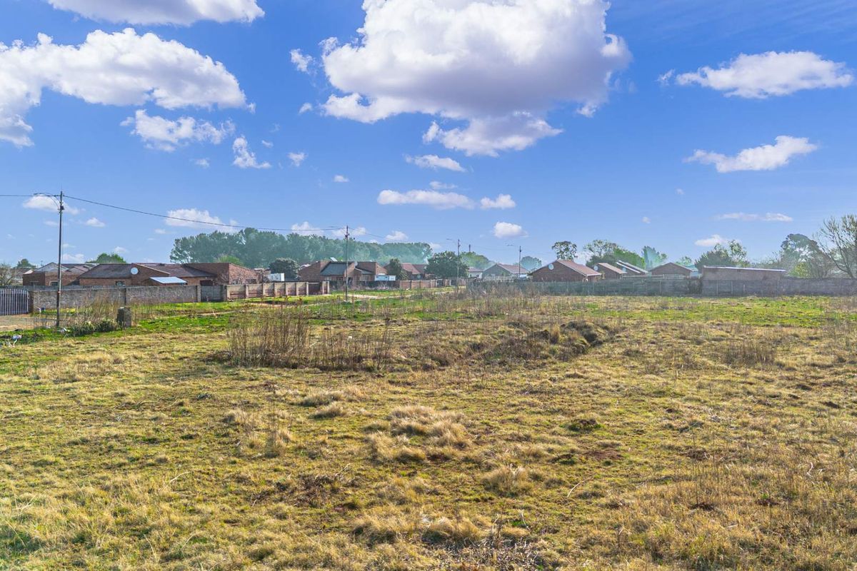 A wide-angle view of an undeveloped plot of land with surrounding residential properties and boundary walls visible in the background.