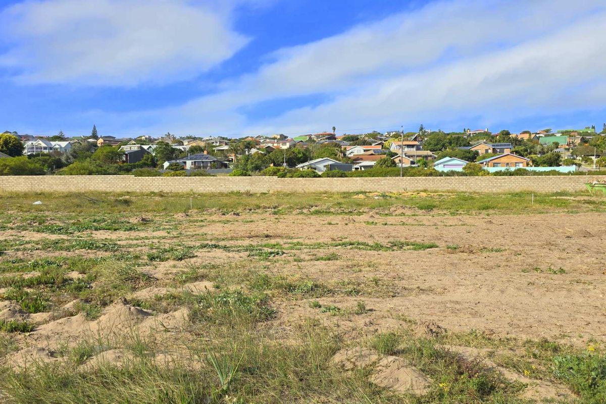 A vacant plot of land featuring natural ground cover and a perimeter boundary wall, offering a clear view of the surrounding residential neighborhood.