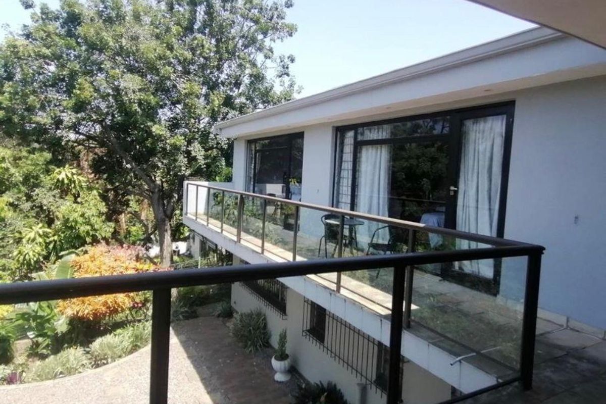 An elevated balcony featuring a modern glass balustrade and sliding door access, overlooking a lush garden area.
