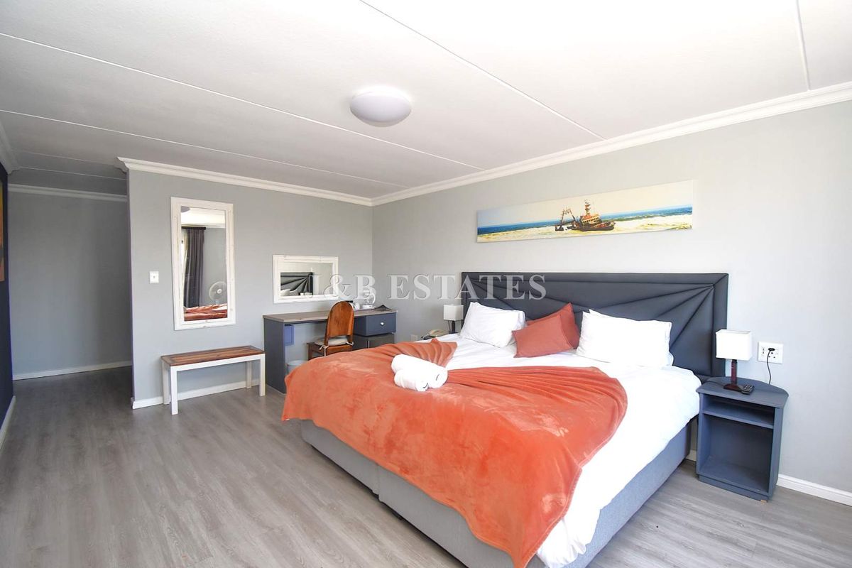 A well-maintained hotel bedroom featuring light grey laminate flooring, neutral wall tones, and a built-in desk area with a wall-mounted mirror.