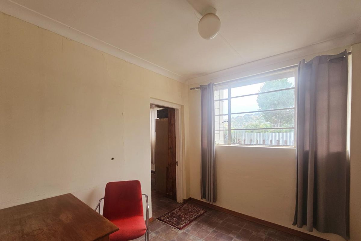 A bedroom featuring tiled flooring, a large window with natural light, and a doorway leading to an adjacent room.