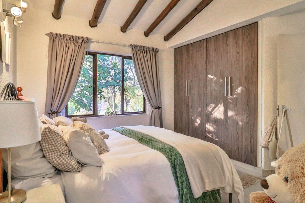 A cozy bedroom featuring exposed timber ceiling beams and built-in wooden wardrobes, offering a warm and inviting atmosphere with natural light.