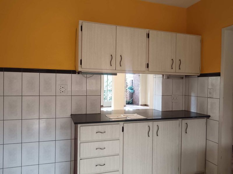 A functional kitchen area featuring laminate cabinetry, dark stone countertops, and tiled splashbacks, offering a blank canvas for potential modern updates.