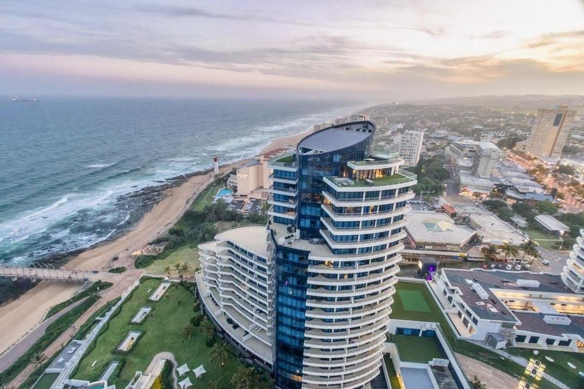 Aerial view of a modern high-rise penthouse building situated along the coastline, showcasing its architectural design and proximity to the ocean.