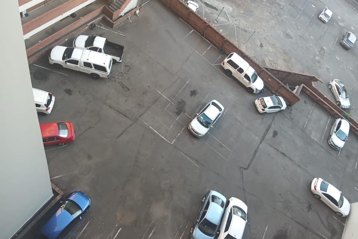 An aerial view of an apartment complex parking area featuring asphalt paving and a brick boundary wall.