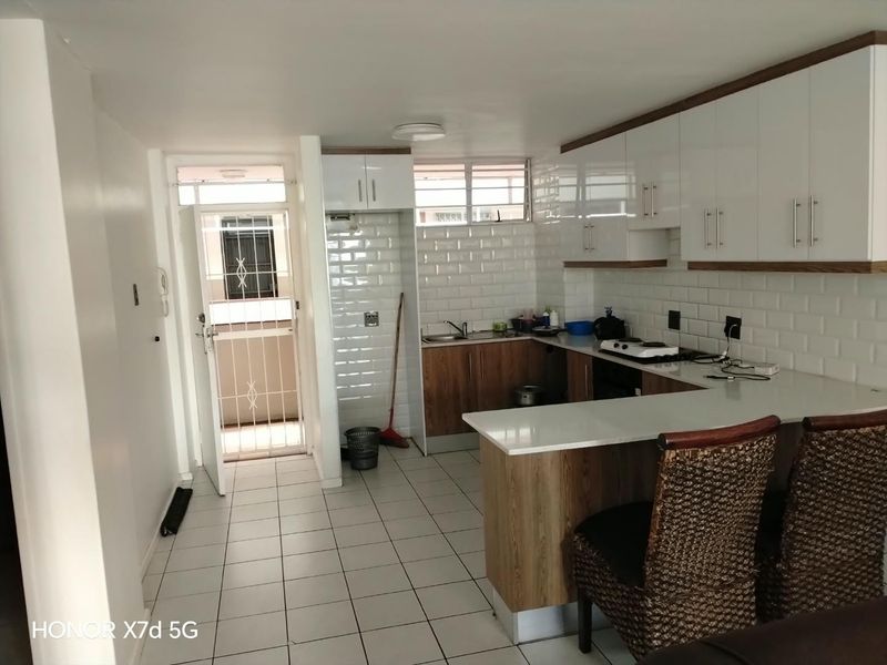 A functional kitchen featuring white subway tile backsplash, modern laminate cabinetry, stone countertops, and direct access to an exterior security gate.