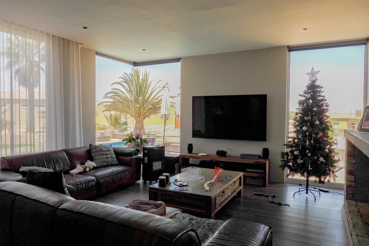 Spacious living room featuring large floor-to-ceiling windows, recessed lighting, and a built-in fireplace, offering seamless views of the outdoor pool area.