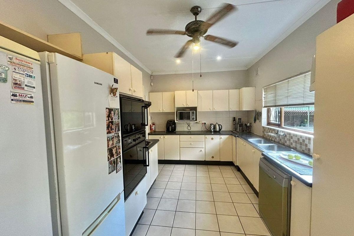 A functional kitchen featuring cream-colored cabinetry, built-in oven, double sink, and tiled flooring, offering a practical layout for daily meal preparation.